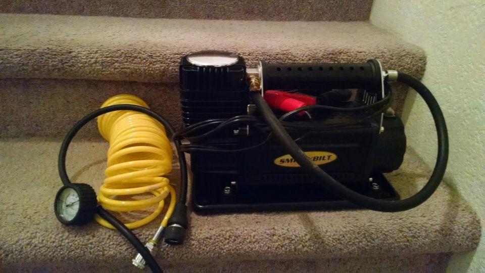 Portable air compressor with yellow coiled hose and tire gauge
