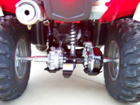 1984 Honda ATC 250 R - Close-up view of the rear axle, suspension, and exhaust system of a red all-terrain vehicle.