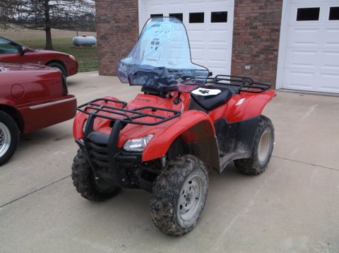 1984 Honda ATC 250 R - A red ATV with a clear windshield is parked in front of a garage, with another red car to its left.