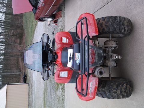 1984 Honda ATC 250 R - A red ATV is parked outdoors next to a red car that has its hood open.