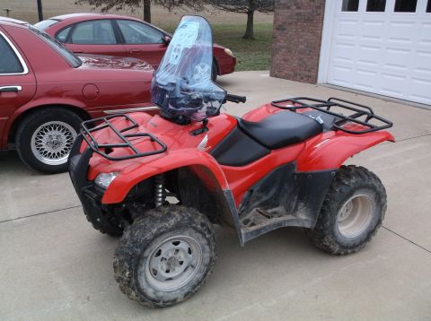 1984 Honda ATC 250 R - A red ATV with a windshield and cargo racks sits on a concrete driveway next to a red sedan.