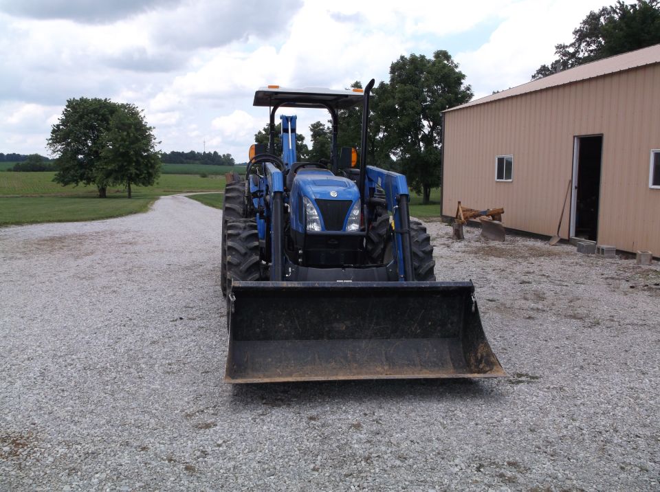 Blue tractor with front loader parked on gravel in front of a tan building