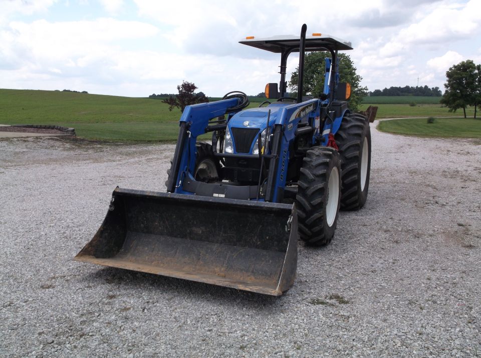 Blue tractor with a front loader attachment parked on a gravel surface