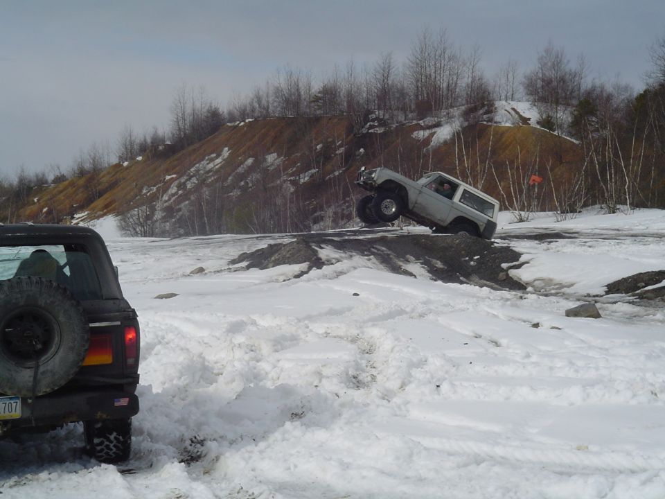 White 1993 Ford Bronco cresting a snowy hill, with another SUV visible in the foreground