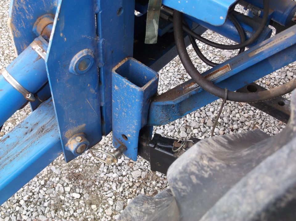 Close-up of blue tractor attachment with hydraulic hoses and a tire visible