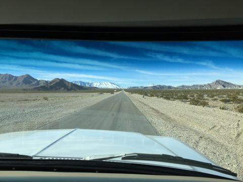 1979 Ford Bronco - Driving down a long, straight road through a desert landscape with mountains on the horizon.