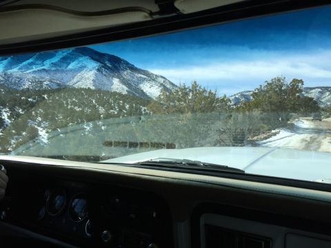 1979 Ford Bronco - Driving through a snowy mountain pass, with a view of the road ahead and distant peaks.