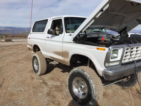 1979 Ford Bronco - This white 1978 Ford Bronco is shown with its hood open, covered in mud, on a dirt road.