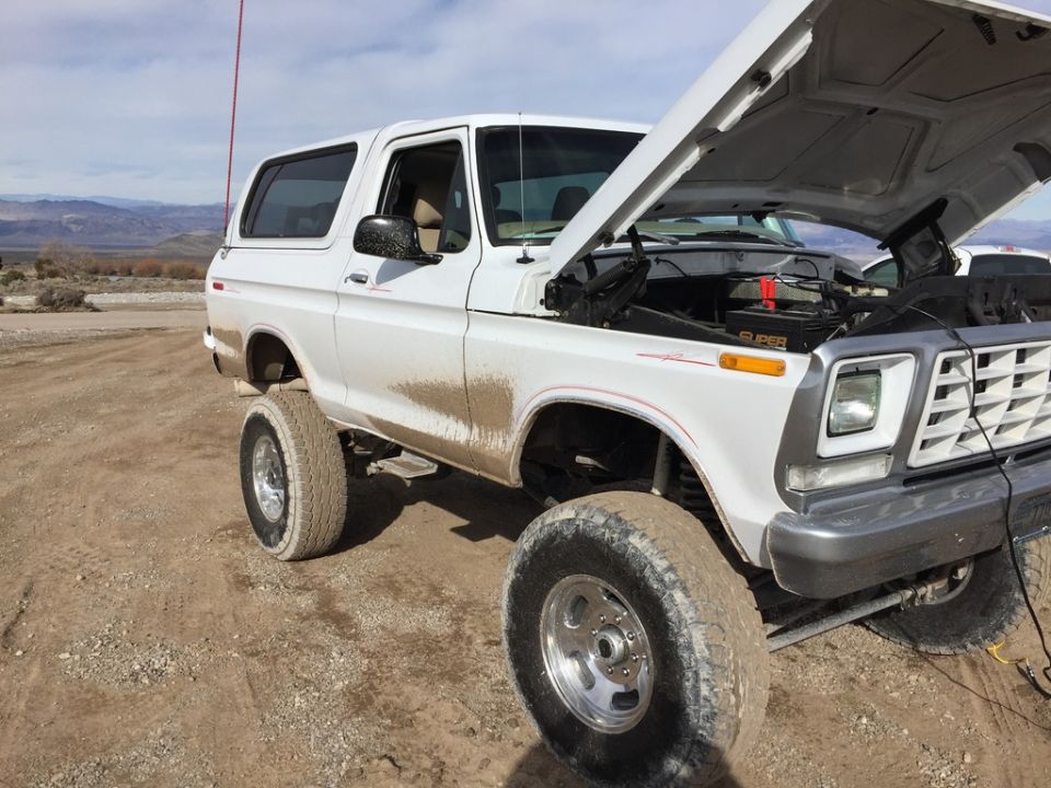 White 1978 Ford Bronco with hood open, covered in mud, parked on a dirt road
