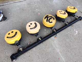 1986 Ford Bronco - A KC lightbar assembly with five lights, some "Daylighter" and smiley face designs, is shown mounted on a black bar.
