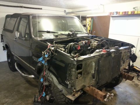 1994 Ford Bronco - This black Ford Bronco is undergoing repairs in a garage, with its engine compartment open and front end disassembled.