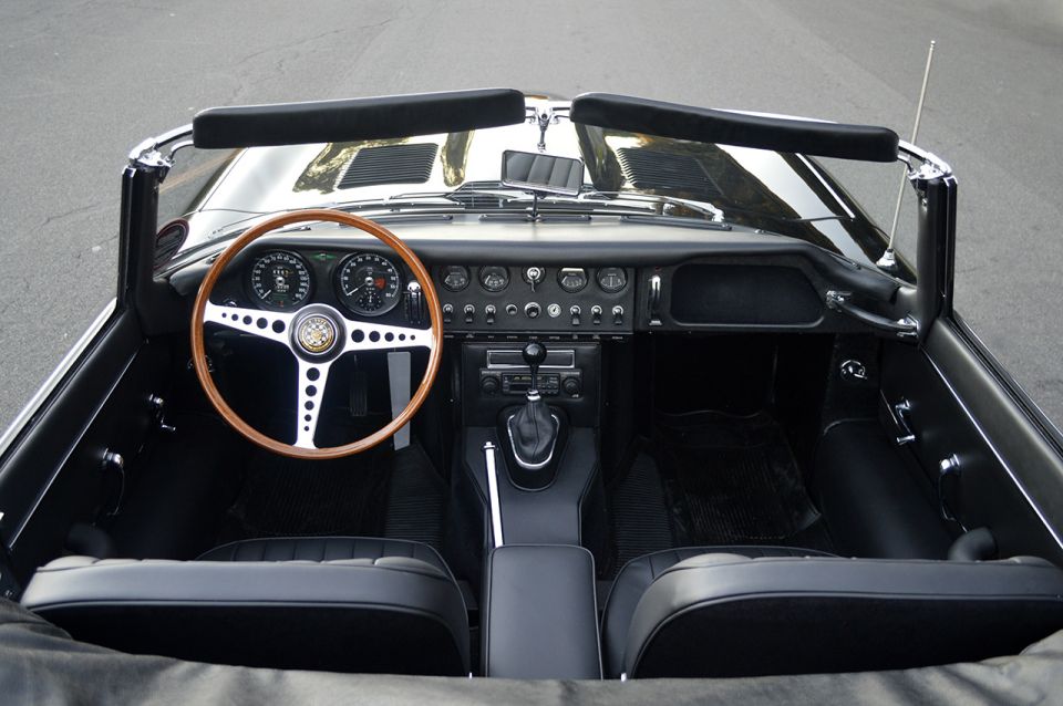Top-down interior of black Jaguar E-Type convertible with wood steering wheel and toggle-switch dash