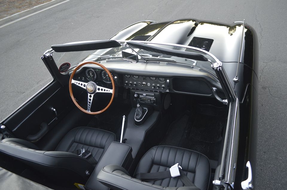 Overhead view of black Jaguar E-Type roadster interior with wood steering wheel and black leather seats
