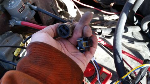 1981 Ford Bronco - Close-up of a hand holding electrical connectors, with engine bay components visible.