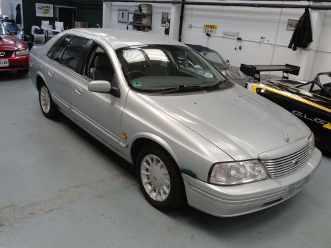 1999 Ford Fairlane - A silver sedan is parked indoors next to other vehicles.