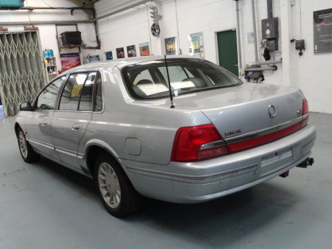 1999 Ford Fairlane - This silver sedan is parked indoors, showing its rear end with distinctive taillights and chrome trim.