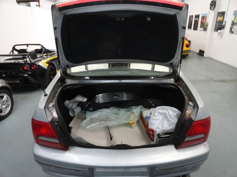 1999 Ford Fairlane - The rear view of a silver sedan shows its trunk open, revealing stored items and a glimpse of other vehicles in the garage.