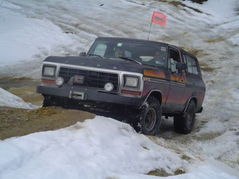1993 Ford Bronco - Dark Ford Bronco with an orange stripe navigates a snowy and muddy incline, equipped with a front-mounted winch.