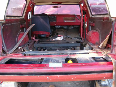 1979 Ford Bronco - The interior of a red 1979 Ford Bronco shows signs of wear and tear, with the rear seats removed.