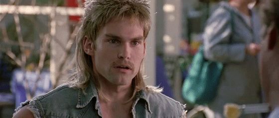 Film still of a man with a blond mullet in a denim vest