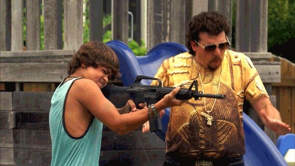 Two men on a playground, one holding a rifle.