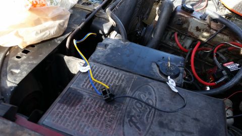 1981 Ford Bronco - Close-up view of a Ford battery in an engine bay, with yellow and blue wires connected to a black electrical component.