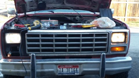 1981 Ford Bronco - The front of a red 1981 Ford Bronco with the hood open, showing engine components and tools. The headlights and turn signals are illuminate…