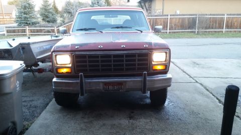 1981 Ford Bronco - The front view of a red 1981 Ford Bronco with its headlights and amber turn signals illuminated. The vehicle is parked on a concrete drivew…