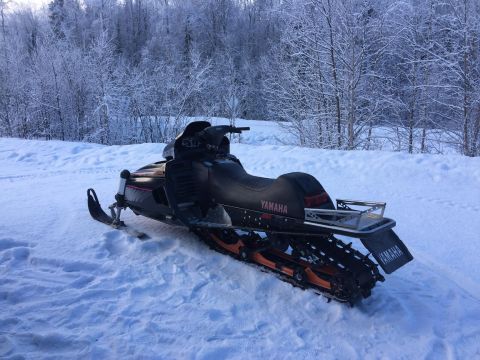 2000 Ford E350 - A black Yamaha snowmobile is parked in the snow with a wooded area covered in frost in the background.
