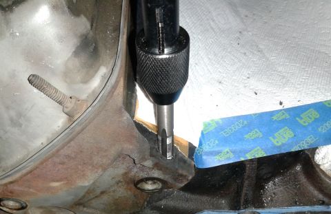 1996 Ford Bronco - A close-up view shows a tap being used to thread a hole in a rusty metal engine component. Blue painter's tape is applied to the surface to…