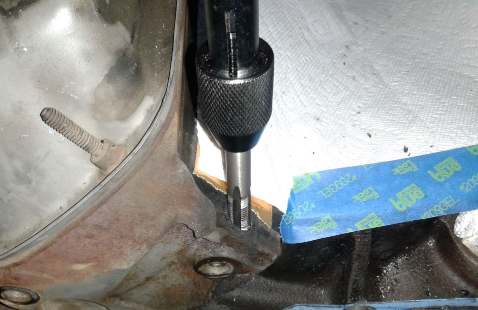 Close-up of a tap threading a hole in a rusty engine part with blue tape.