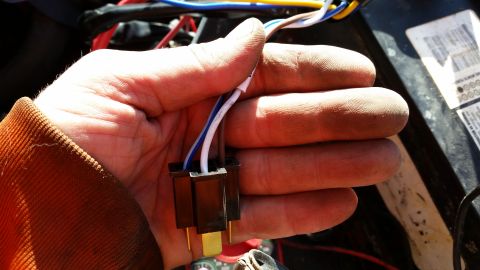 1981 Ford Bronco - A hand holds a black electrical connector with three wires (white, blue, and brown) leading into it. The connector has three gold-colored p…