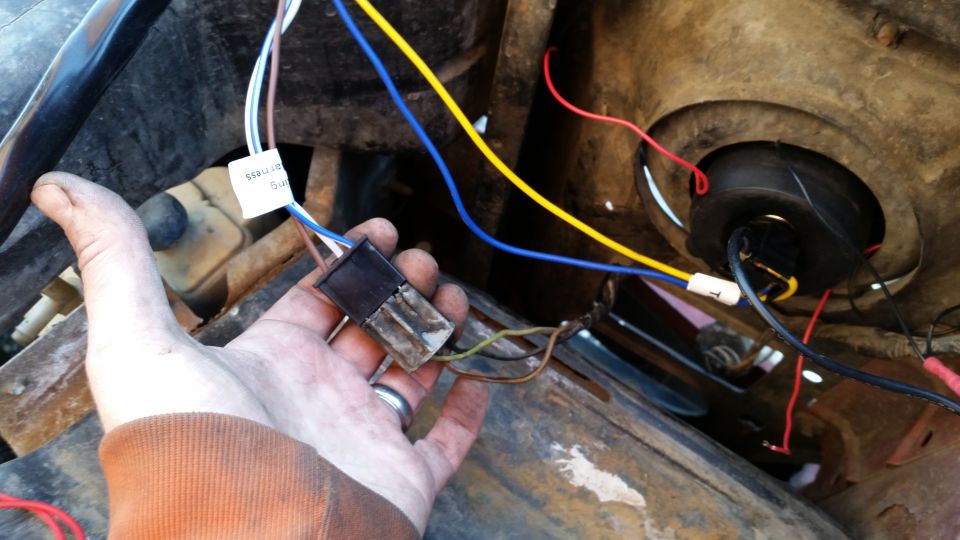 Hand holding a wiring harness connector with blue, yellow, brown, and white wires.