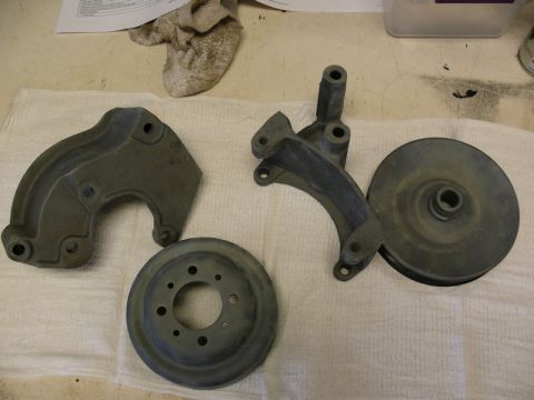 Automotive parts: pulley, bracket, and brake rotor on a white cloth.