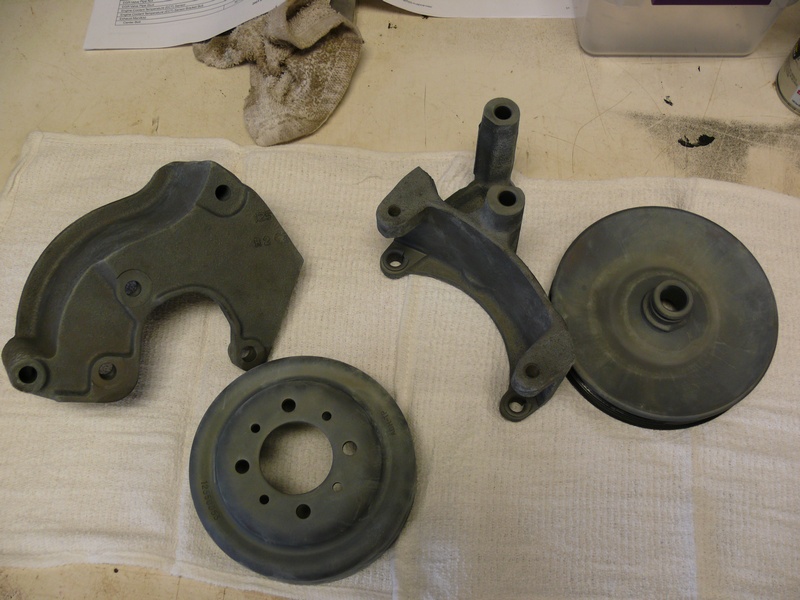 Automotive parts: pulley, bracket, and brake rotor on a white cloth.