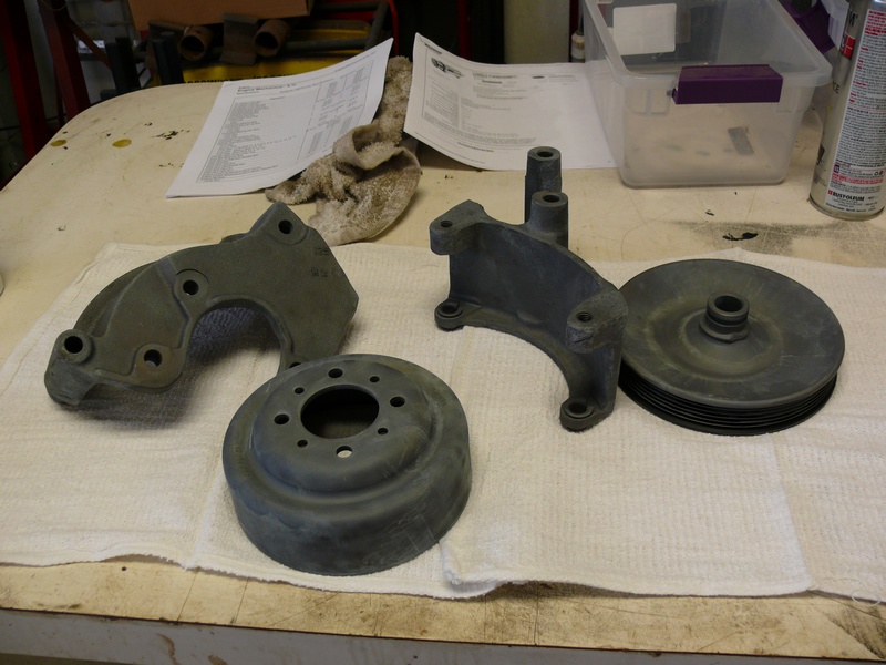Automotive parts including a pulley, bracket, and disc with holes on a white towel.