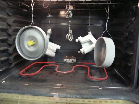 Two metal parts hanging in an oven with a red heating element.