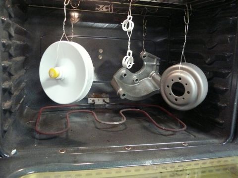 Three automotive parts hanging in an oven for coating.