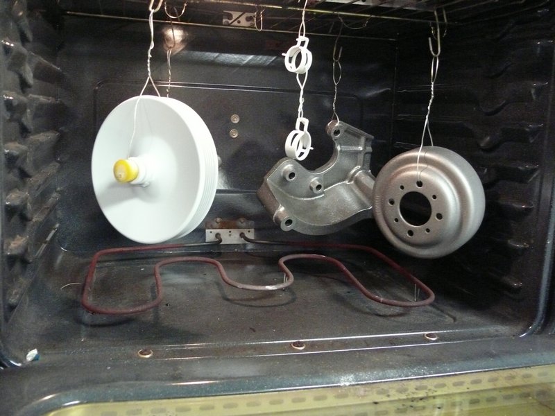 Three automotive parts hanging in an oven for coating.