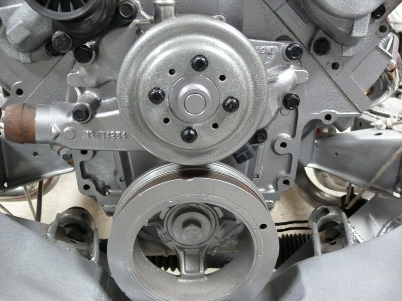 Silver engine block with water pump and crankshaft pulley, showing part number.