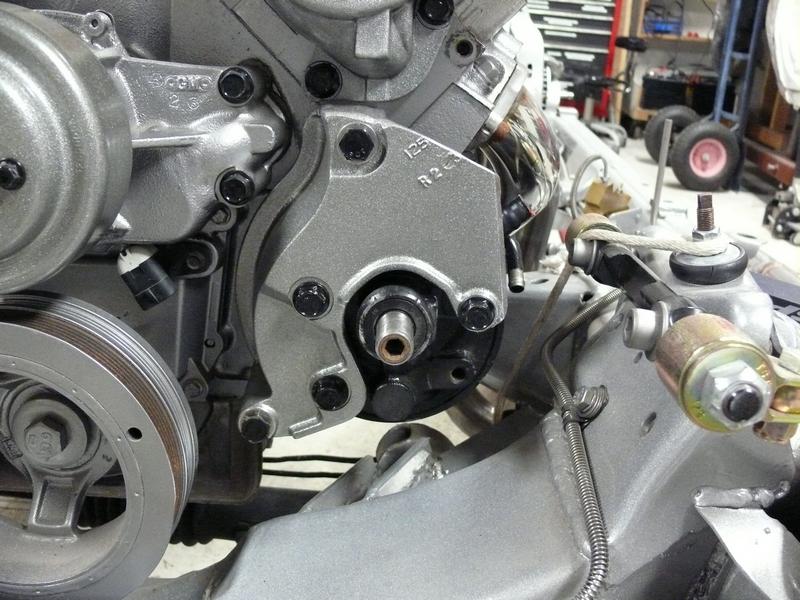 Silver engine component with pulleys and bolts attached to vehicle chassis