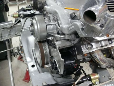 Close-up of a silver engine assembly with water pump, pulley, and exhaust manifold. Yellow pencil on top.