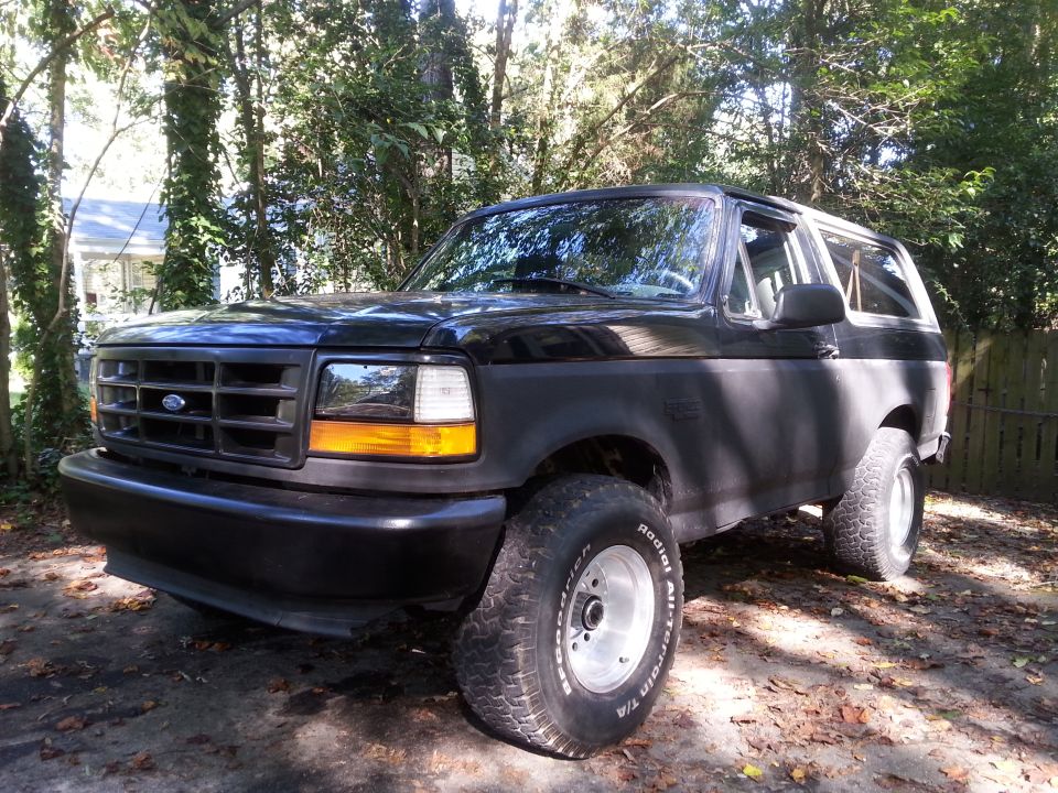 Black 1994 Ford Bronco parked outdoors with trees and fallen leaves.