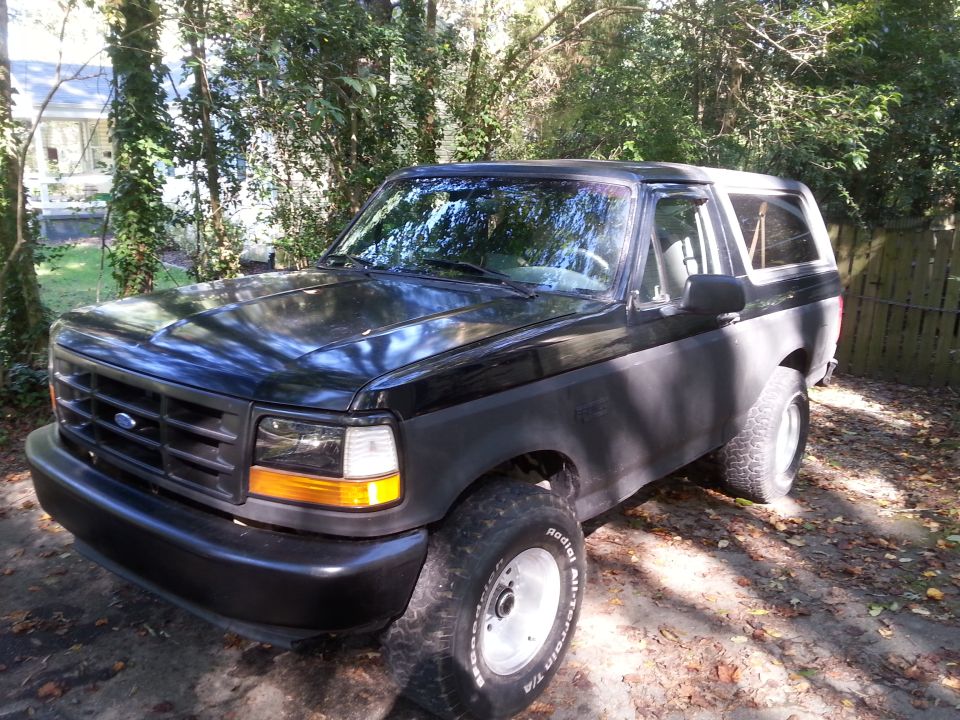 Black Ford Bronco parked outdoors with trees and foliage in the background.