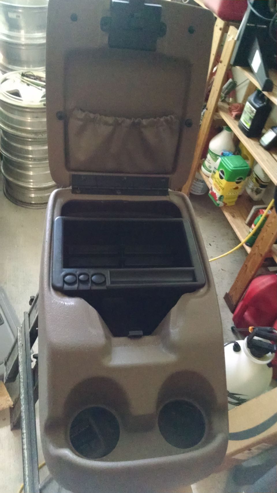 Tan center console from a 1995 Ford Bronco, open, showing storage and cup holders.