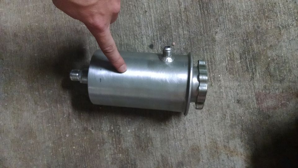 Shiny metal cylindrical reservoir with a cap and fitting, resting on concrete.