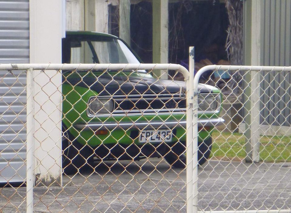 Green and black vintage car with license plate FPL435 behind a chain-link fence.