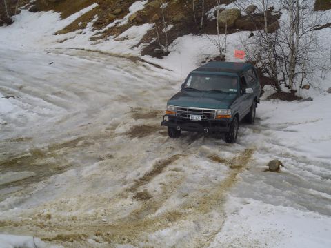 1993 Ford Bronco - A green SUV navigates a challenging snowy and muddy terrain.