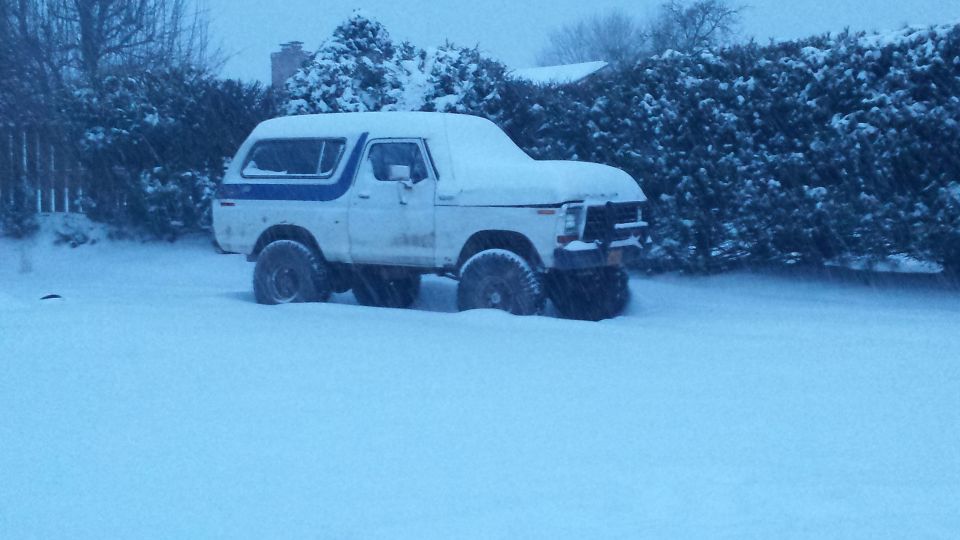 White 1979 Ford Bronco with blue stripe parked in deep snow during a blizzard.