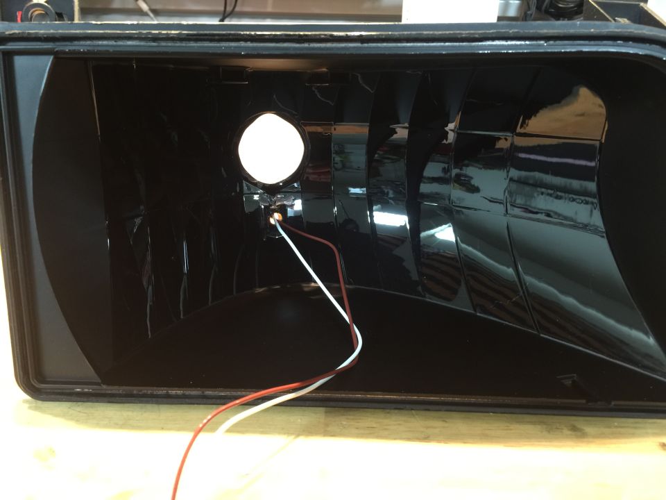 Black headlight interior with reflective facets and two wires connected to a light.